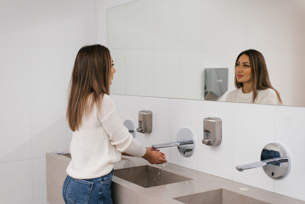 Woman washing her hands in a bathroom - highlighting the need for feminine waste collection | sanitary waste collection